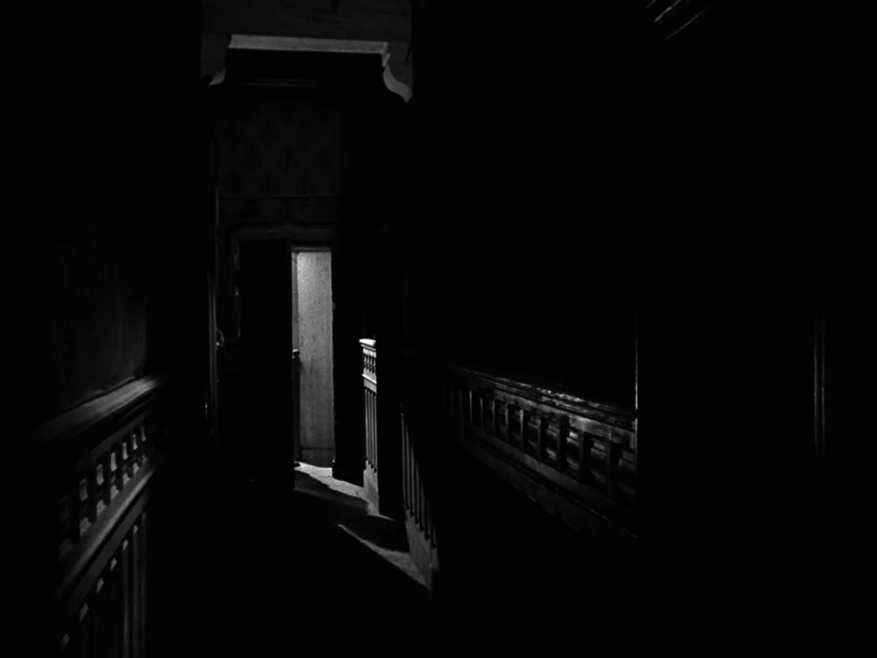 Diabolique (1955) movie still: establishing — A narrow residential hallway features wooden paneling and a dark, patterned wall surface. A single…
