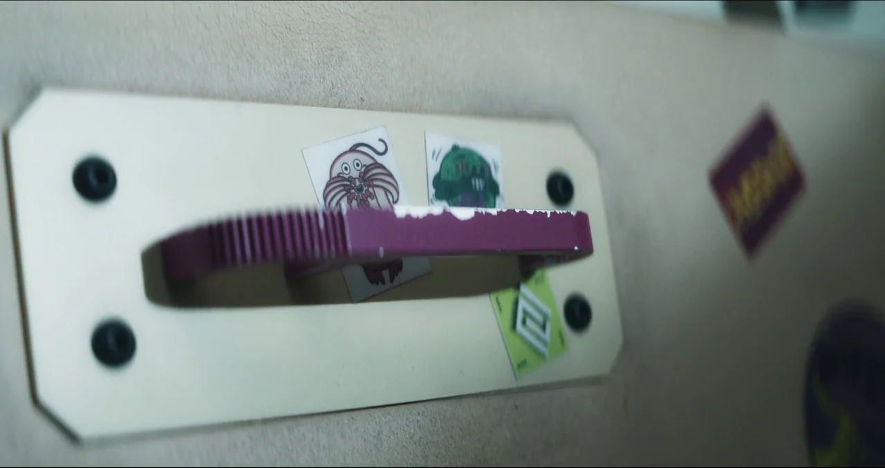 Prospect (2018) movie still: closeup — A close-up of a metal locker door with a chipped purple handle attached. Several small stickers featuring…
