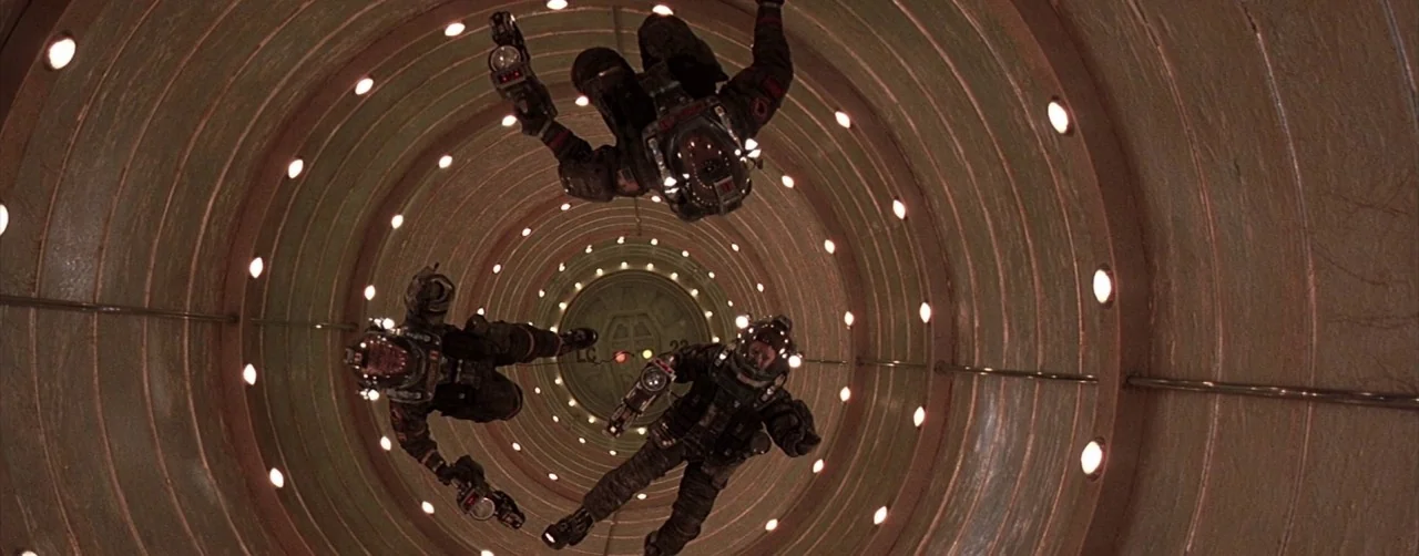 Event Horizon (1997) movie still: wide — A long cylindrical tunnel with a ribbed interior surface features multiple glowing circular lights. Three…