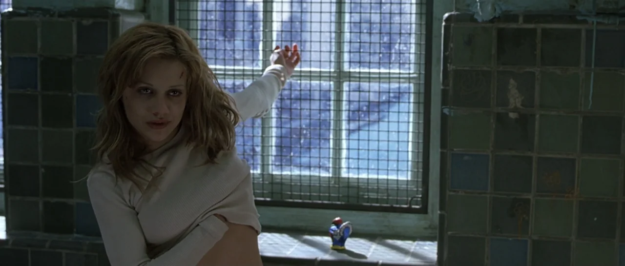 Don't Say a Word (2001) movie still: medium — A tiled room contains a window covered by a heavy wire mesh grate. A woman stands in the foreground…