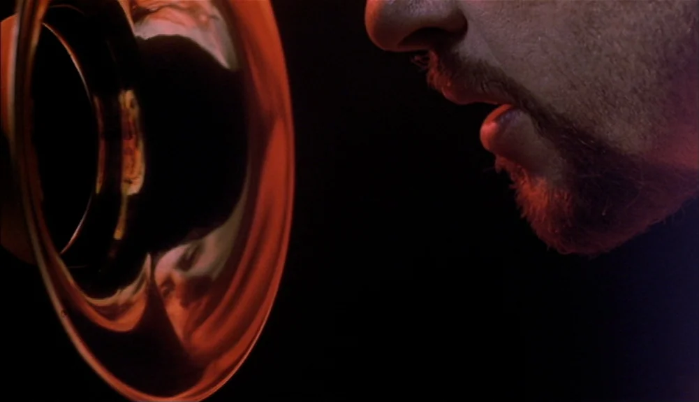 Bram Stoker’s Dracula (1992) movie still: closeup — A man's profile appears in low light against a black background. He blows into the bell of a…