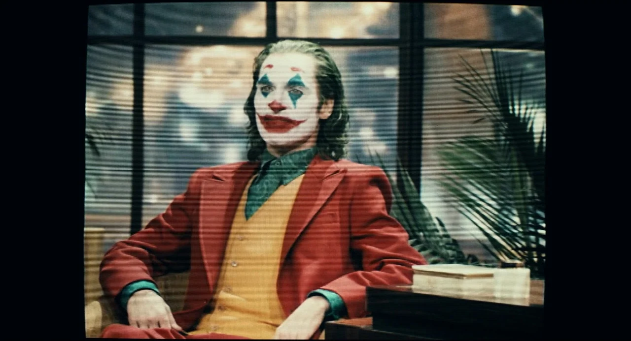 Joker (2019) movie still: medium — A television broadcast studio set features a window background overlooking blurred city lights at night. A man in…