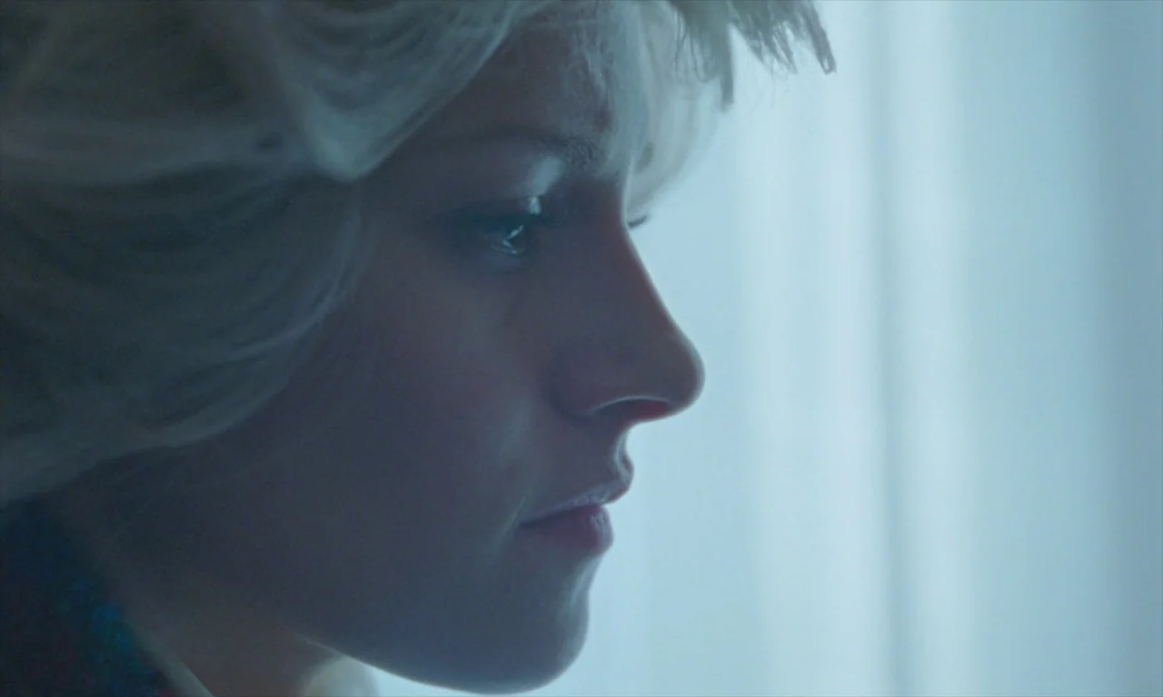Spencer (2021) movie still: closeup — An interior space with a window providing filtered daylight across the frame. A blonde woman appears in side…