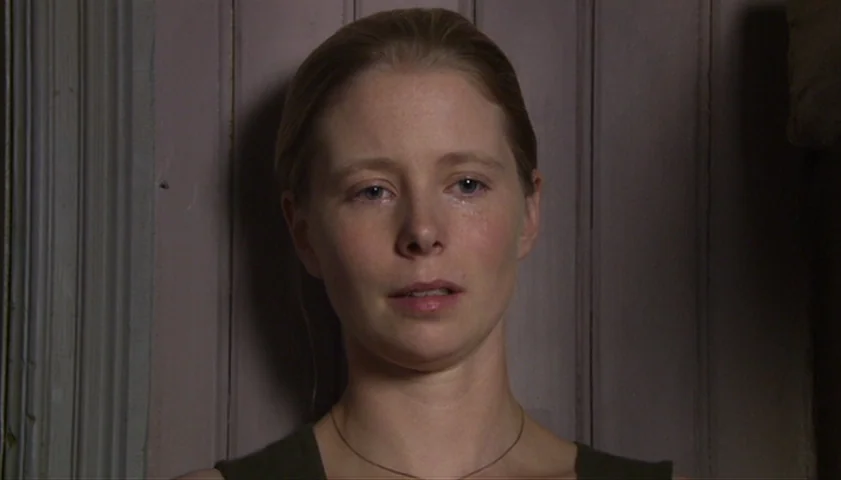Saraband (2003) movie still: closeup — A woman stands before a wall of light-colored vertical wooden paneling. She faces forward with a…