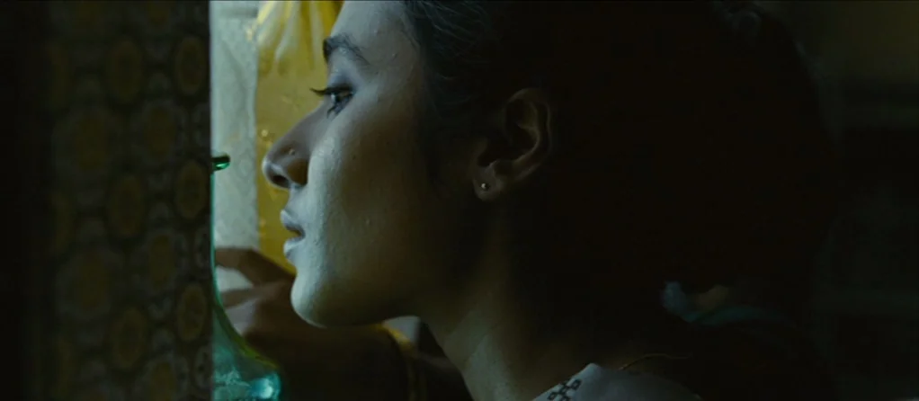 Brick Lane (2007) movie still: closeup — A close view of a person looking through a small gap in a doorway. Light filters through patterned fabric…