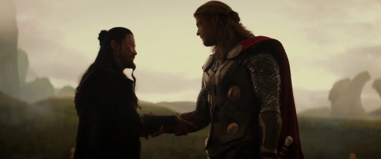 Thor: The Dark World (2013) movie still: medium — An open field under a cloudy, overcast sky with distant rock formations. Two men stand facing each…