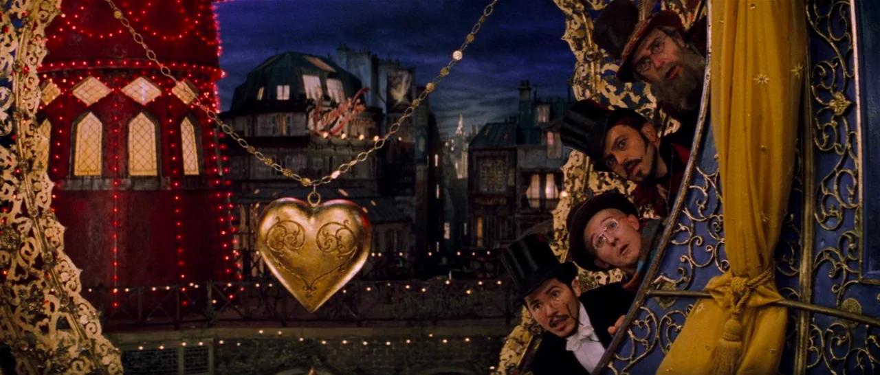 Moulin Rouge! (2001) movie still: wide — A night city view features dark architectural buildings illuminated by decorative red lights and a large…