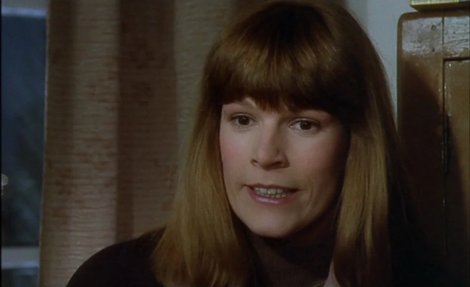 I Want To Go Home (1989) movie still: closeup — A woman stands indoors with brown curtains and a wooden surface visible behind her. She is facing to…