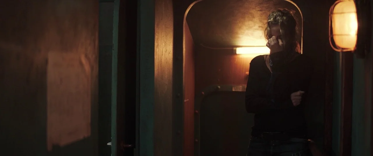 Sea Fever (2019) movie still: medium — A narrow metallic corridor with dark steel surfaces features rounded bulkhead doorways and exposed wiring. A…