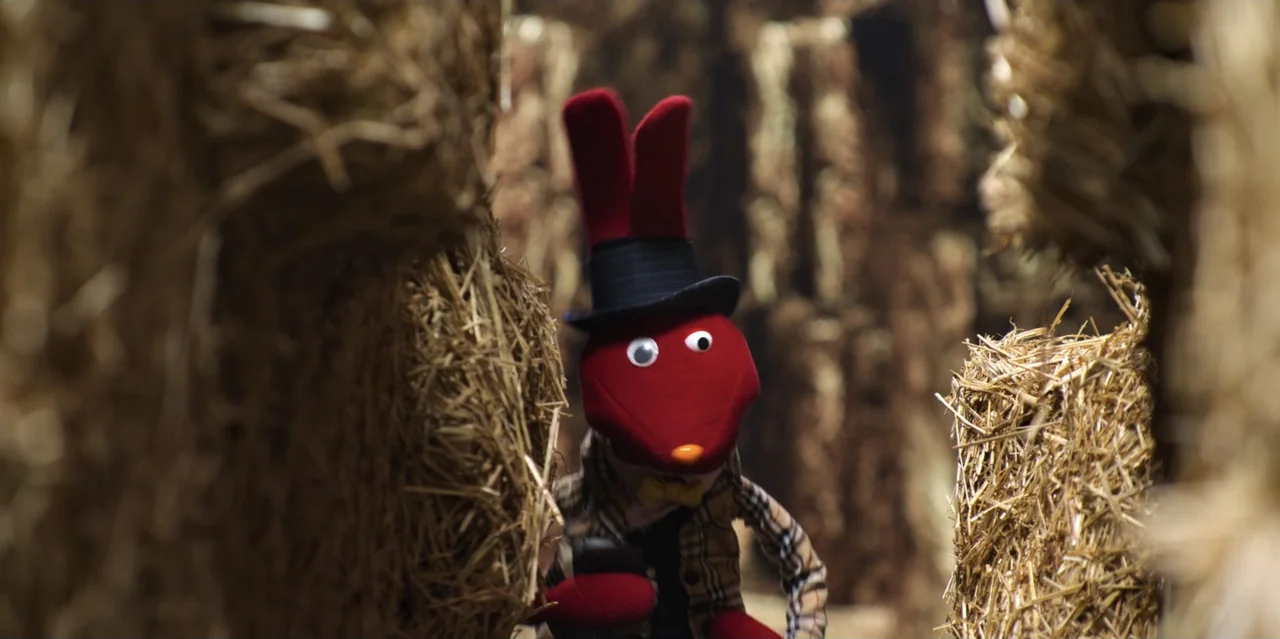 31 Minutes: One Hot Christmas (2025) movie still: medium — A narrow path is formed by tall vertical walls made of stacked dry hay. A red rabbit…