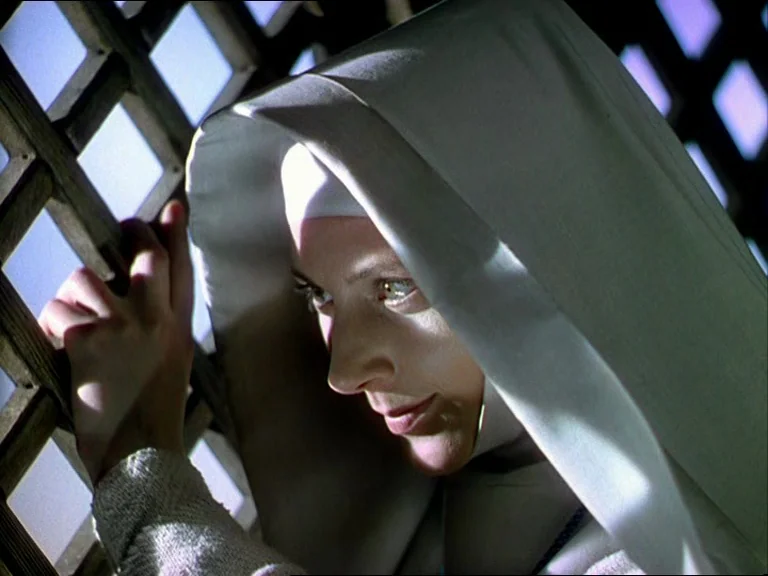 Black Narcissus (1947) movie still: closeup — An interior space features a wooden lattice screen lit by incoming daylight. A woman in a white habit…