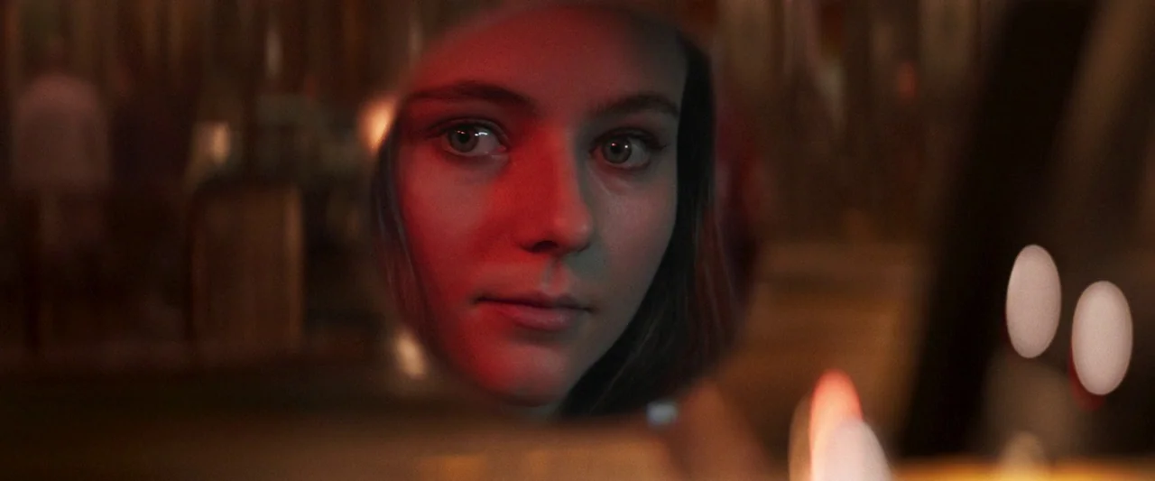 Last Night in Soho (2021) movie still: closeup — A woman's face is centered in a circular reflection within a dark, indistinct environment. She…