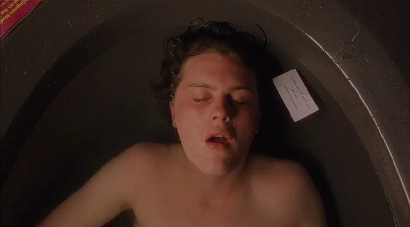 Hedwig and the Angry Inch (2001) movie still: closeup — A person lies submerged in a bathtub surrounded by curved, dark metallic edges. A small…