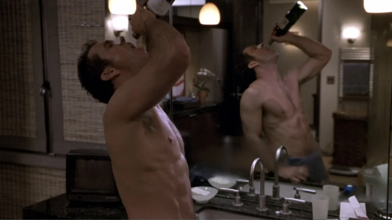 What Women Want (2000) movie still: medium — A modern bathroom vanity with a large mirror and dim ambient lighting at night. A shirtless man tilts…