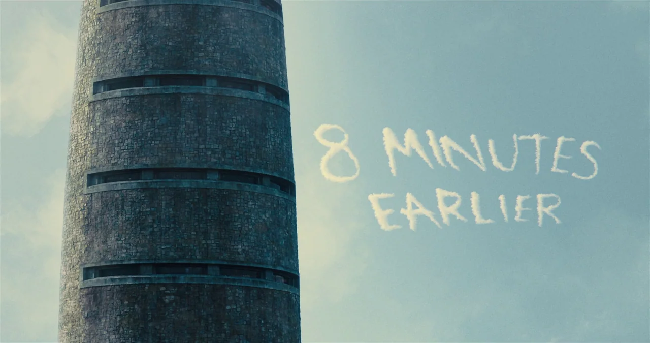 The Suicide Squad (2021) movie still: establishing — A tall cylindrical stone tower stands prominently against a clear, pale blue daytime sky. Wispy…