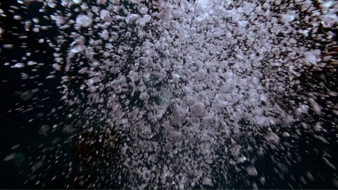 Alien Sharks: Strange New Worlds (2023) movie still: establishing — An underwater perspective shows a dense cloud of rising air bubbles in dark…