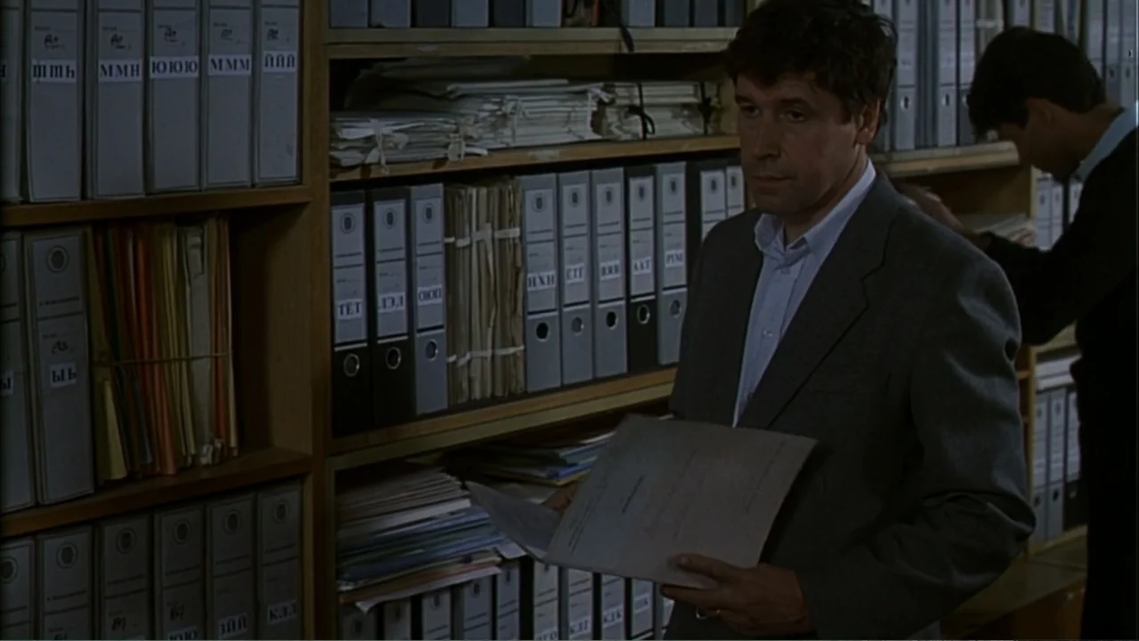 Citizen X (1995) movie still: medium — An archive room filled with wooden shelving units packed with numerous labeled binders. A middle-aged man in…
