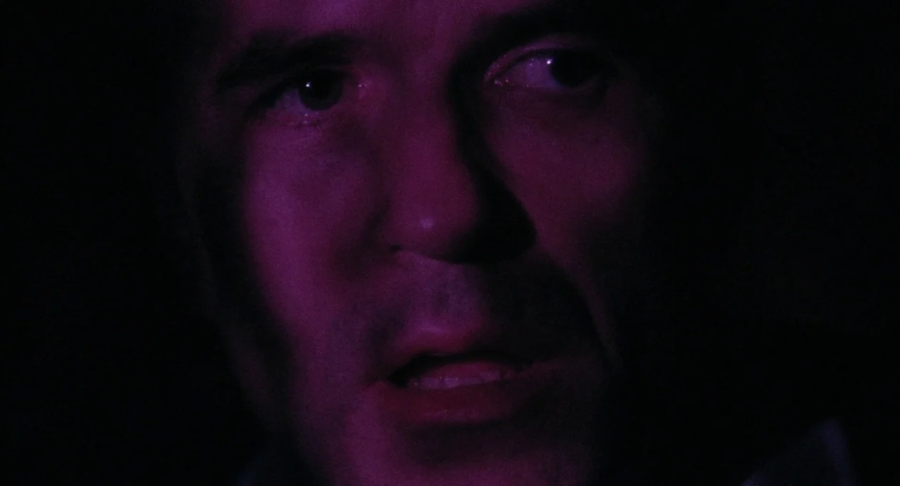 What Happened Was… (1994) movie still: closeup — A dark space lit only by a sharp magenta light on the subject. A man with dark features and stubble…