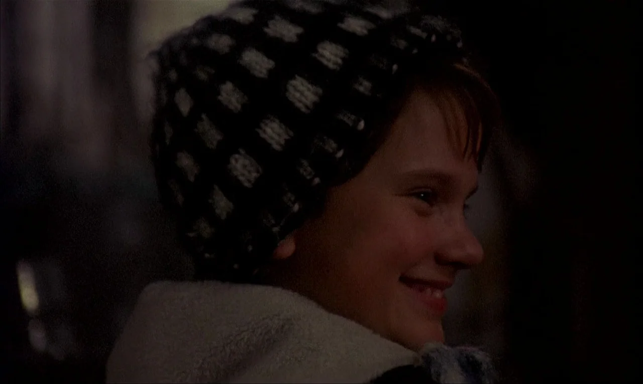 My Life As A Dog (1985) movie still: closeup — A dark outdoor setting at night features a young boy in profile view. The boy wears a winter hat and…