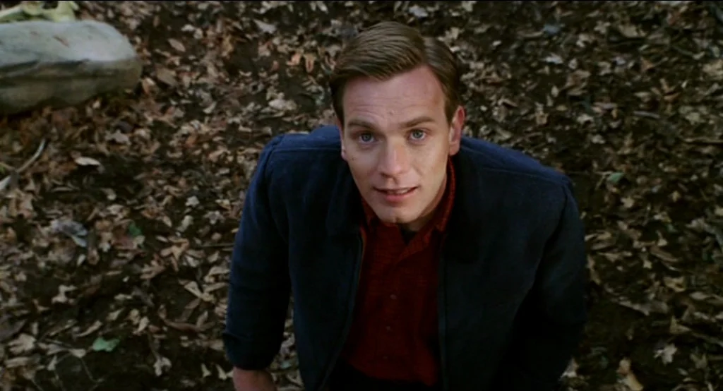 Big Fish (2003) movie still: medium — A man stands outdoors surrounded by a layer of dried brown leaves on the ground. The person looks up toward…