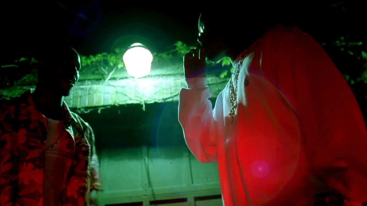 Belly (1998) movie still: medium — Two men stand in front of a garage door at night under colored lights. The scene is illuminated by harsh red and…