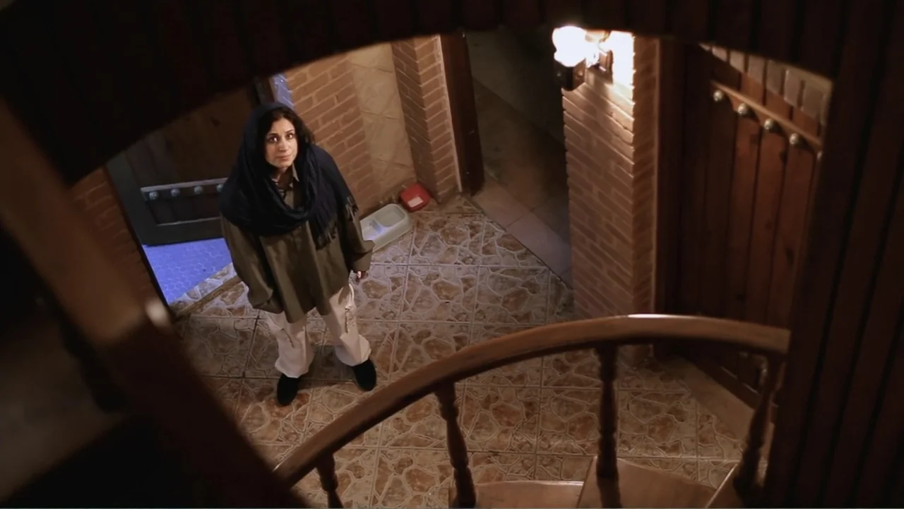 Closed Curtain (2013) movie still: medium — A tiled interior landing features brick-accented walls and a wooden staircase railing. A woman wearing a…