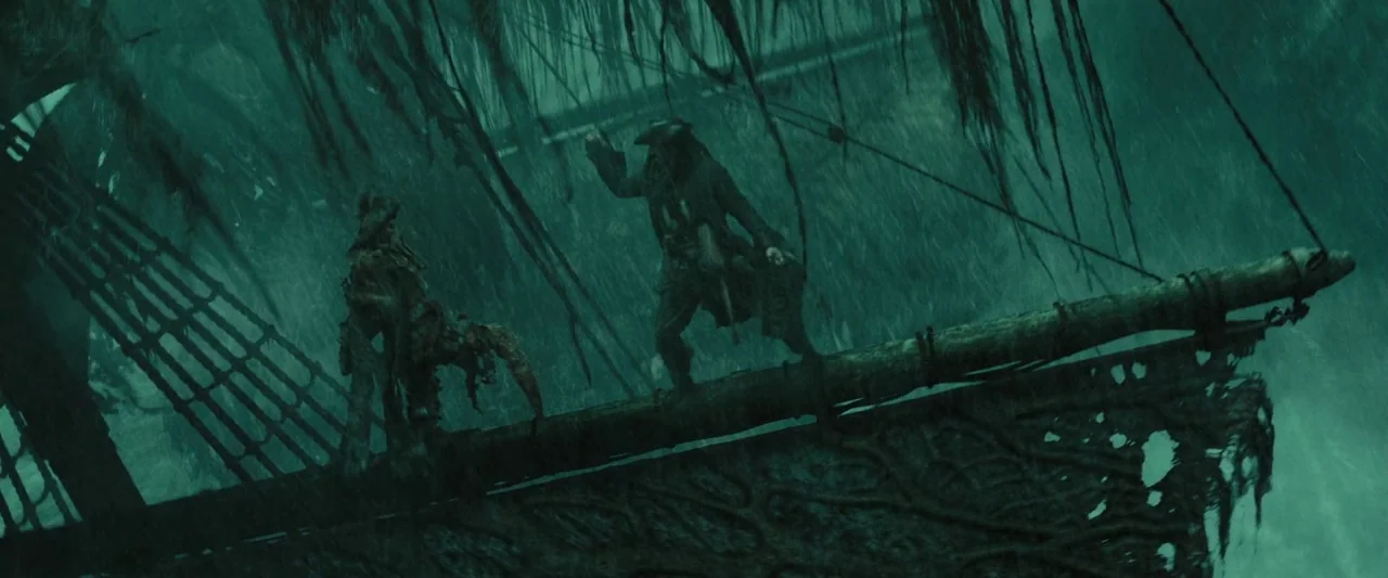 Pirates of the Caribbean: At World’s End movie still: wide — A dark, storm-swept wooden ship bowsprit is slick with rain in the night. Two figures…