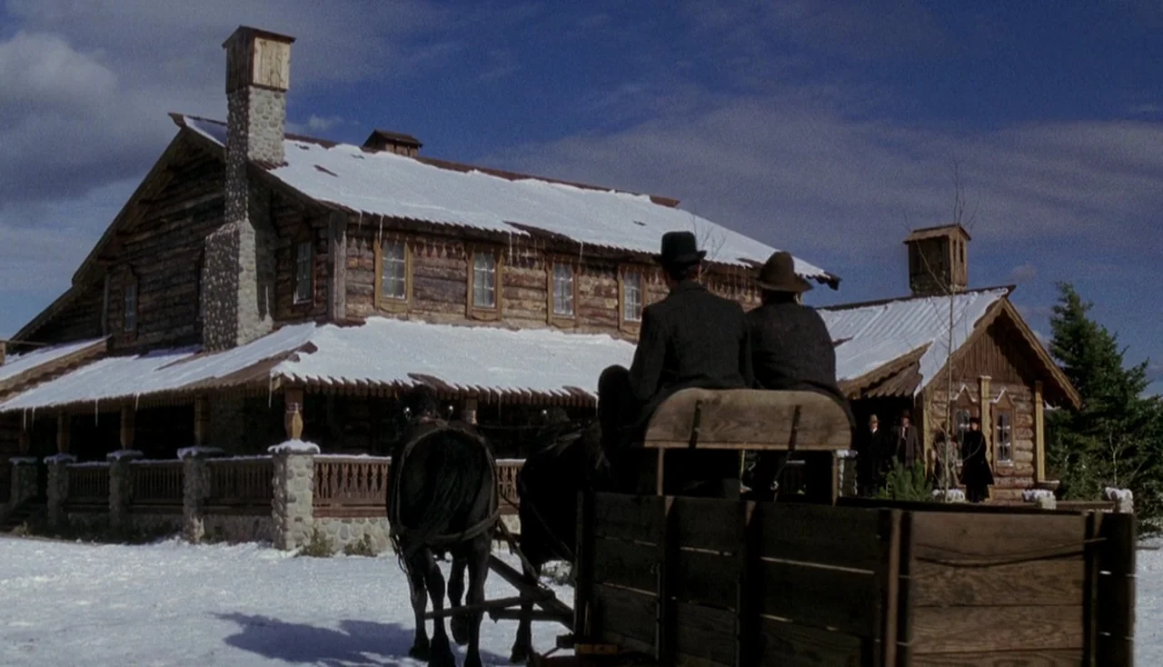 Legends of the Fall (1994) movie still: wide — A large two-story log lodge sits in a snowy field under a clear blue sky. Two men ride in a wooden…