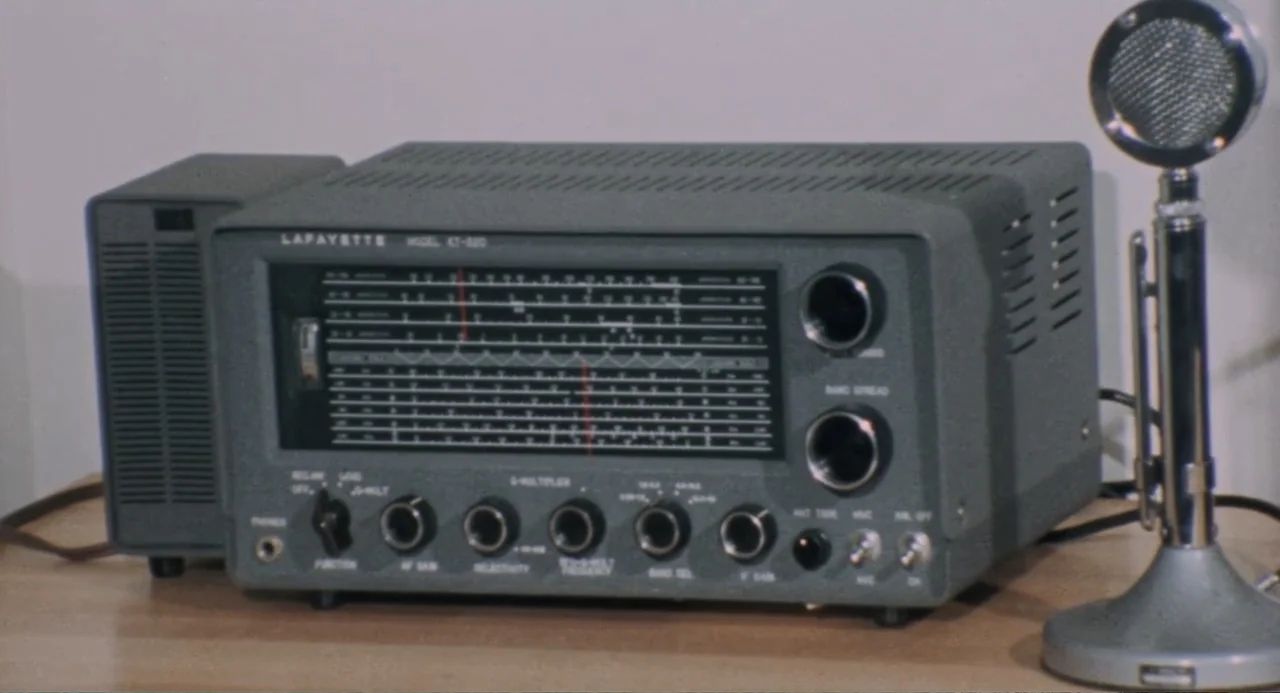 The Last House on the Left (2009) movie still: closeup — A vintage grey Lafayette radio receiver sits on a flat wooden desk surface. A silver metal…