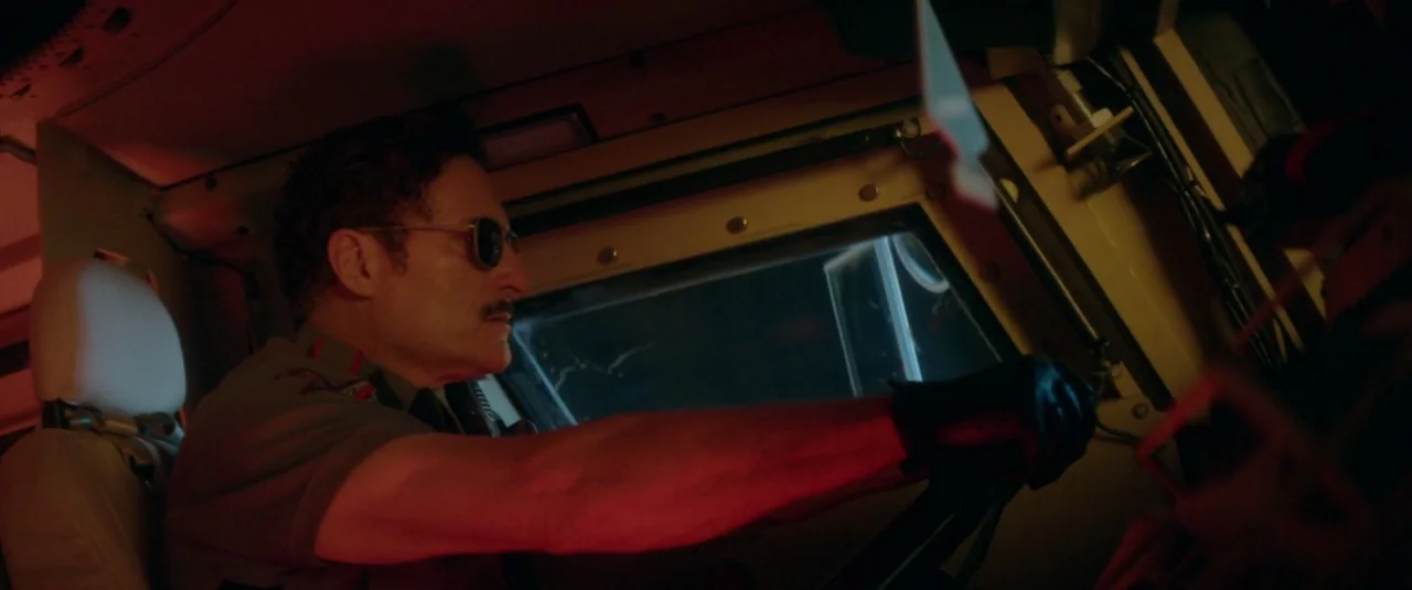 Officer Downe (2016) movie still: medium — Inside the cabin of a truck at night, illuminated by a red interior light. A man with a mustache and…