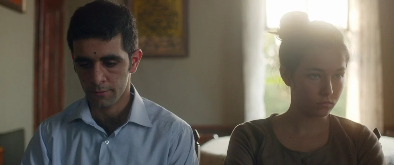 Mustang (2015) movie still: medium — A quiet room with soft natural light streaming through a bright window behind two people. A man and a young…