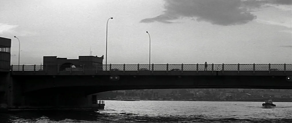 Girl on the Bridge (1999) movie still: wide — A long concrete bridge stretches horizontally across the frame over a wide body of water. A single…