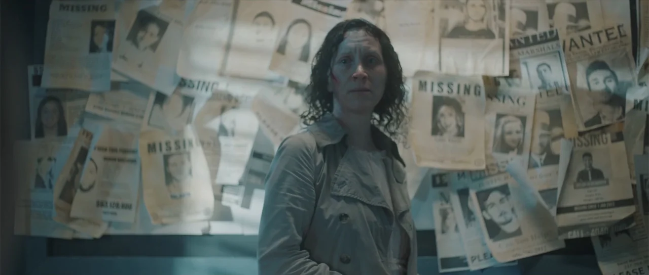 Night of the Missing (2023) movie still: medium — A dimly lit interior room features a wall densely papered with multiple missing person flyers. A…