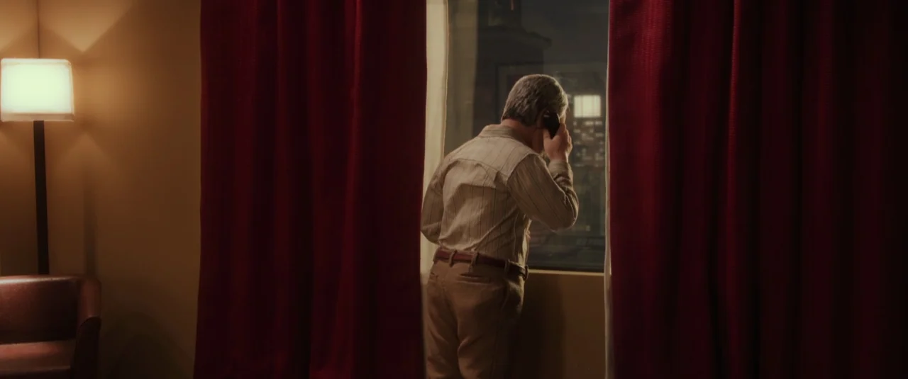 Anomalisa (2015) movie still: medium — An interior space features red heavy curtains flanking a window overlooking a night cityscape. An older man…