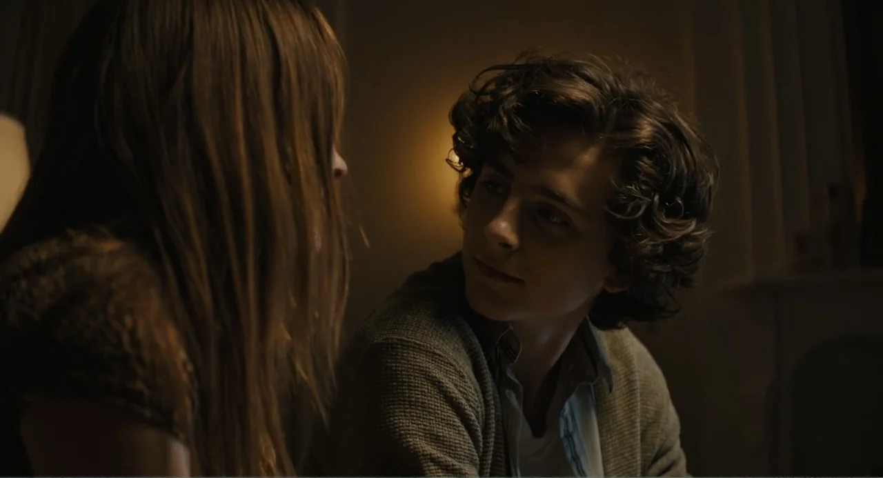 Beautiful Boy (2011) movie still: medium — A dark indoor space illuminated by a single lamp glows softly in the background. A young man with curly…