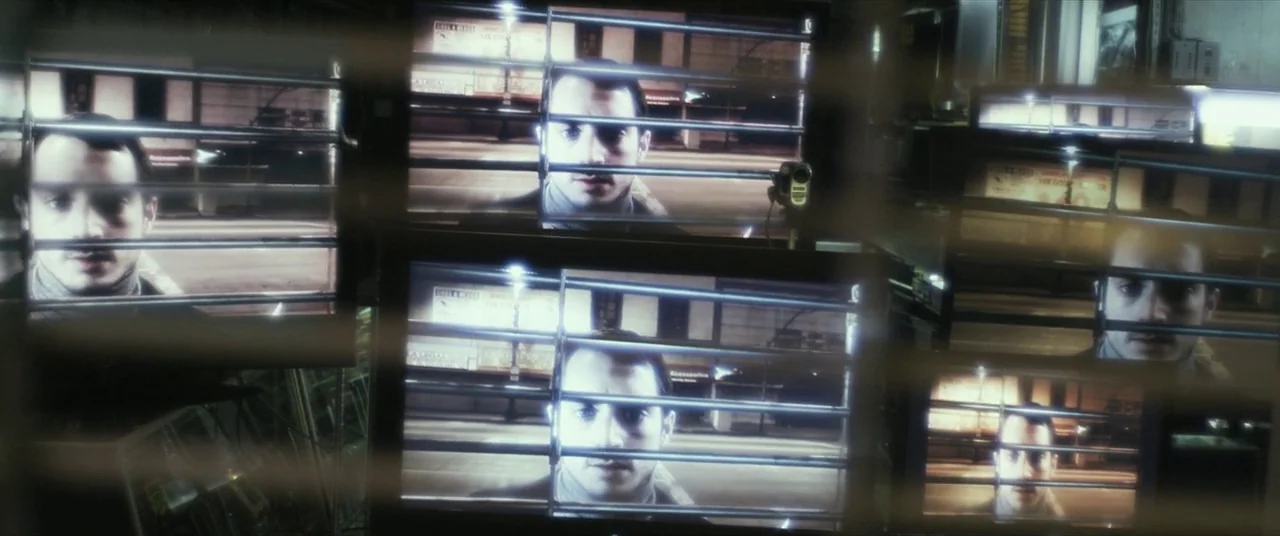 Maniac (2012) movie still: wide — A dark room contains multiple video monitors showing the same man at night. Metal blinds across the foreground…