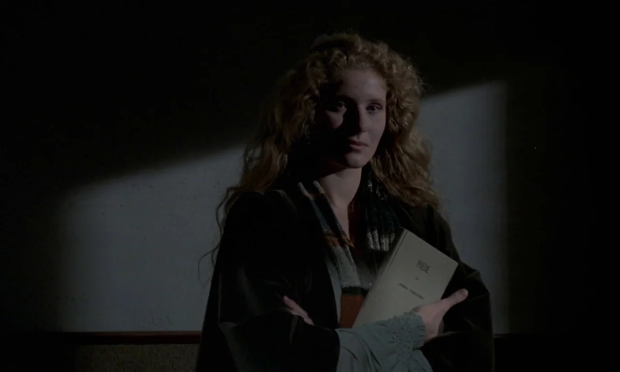 Nostalghia (1983) movie still: medium — A person stands in a dim room with a patch of light on the wall. She holds a book with both hands against…