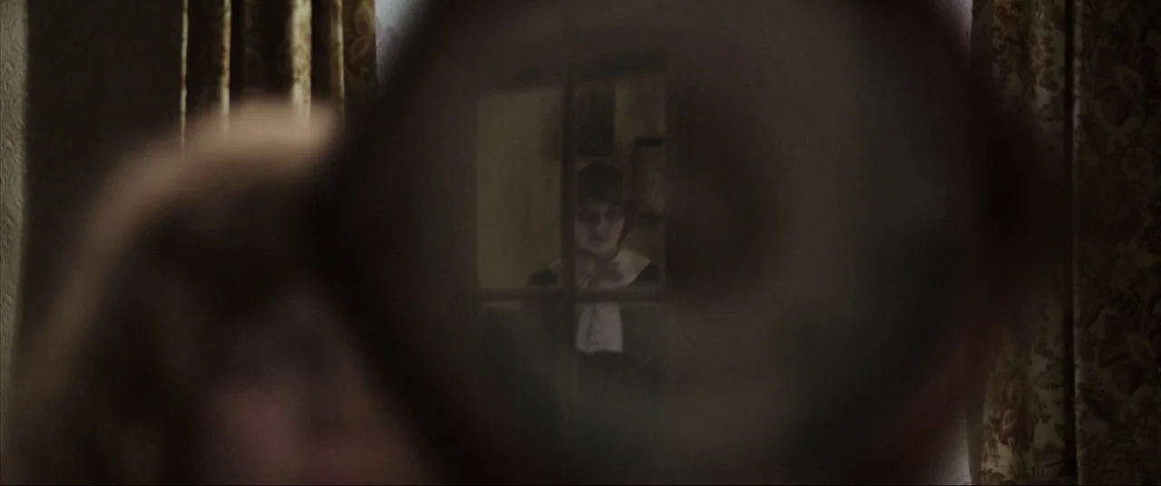 The Conjuring (2013) movie still: closeup — An interior space features patterned fabric curtains and a multi-pane glass door frame. A young boy…