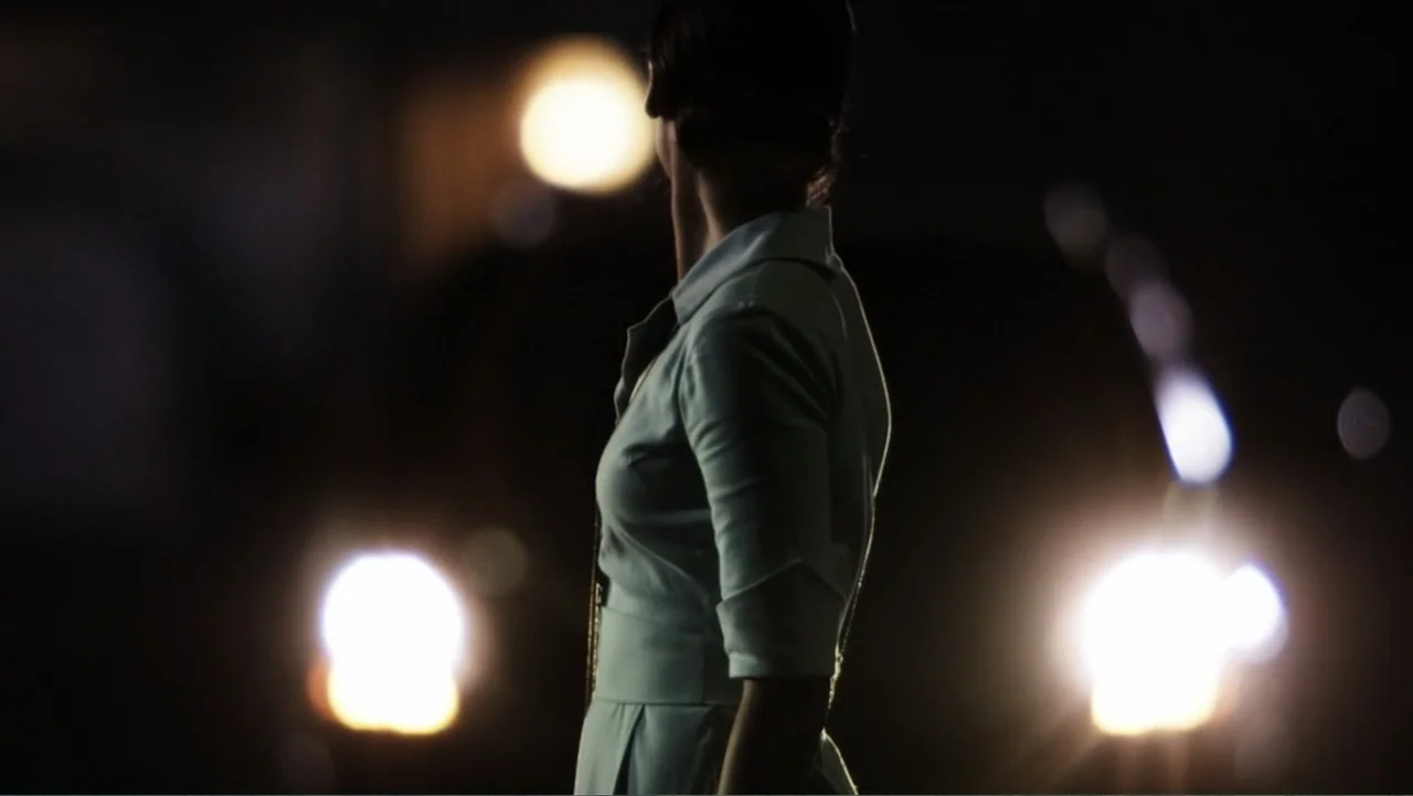 Alice in Marialand (2014) movie still: medium — A dark outdoor space features blurred bright circular light sources in the background. A woman in a…