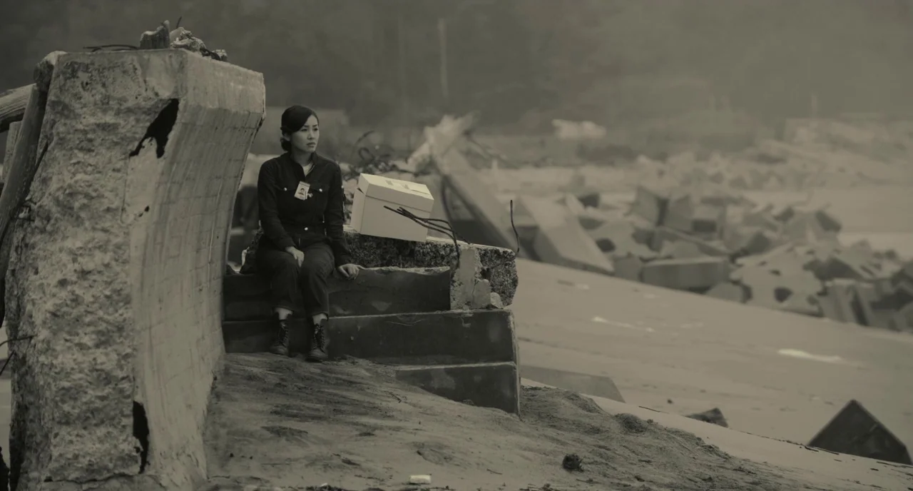 The Whispering Star (2015) movie still: fullbody — A desolate coastline features broken concrete structures and debris scattered across the sandy…