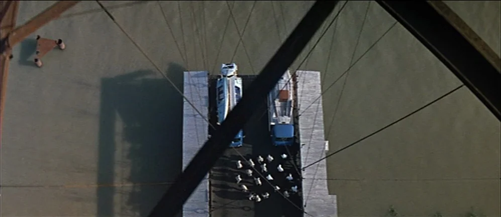 Les Demoiselles de Rochefort (1967) movie still: wide — An aerial view shows a concrete pier surrounded by green water with structural beams. A…