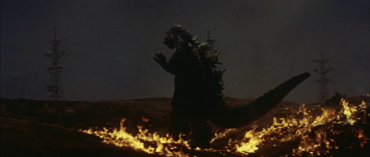 Mothra Vs Godzilla (1964) movie still: wide — A dark night landscape features large electrical towers silhouetted against a murky sky. A massive…