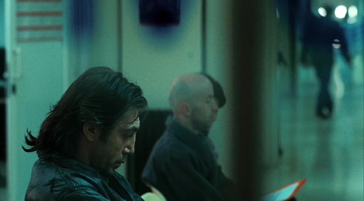 Biutiful (2010) movie still: medium — A man with dark hair sits next to a bald man in a waiting area. They both look downward toward a document…