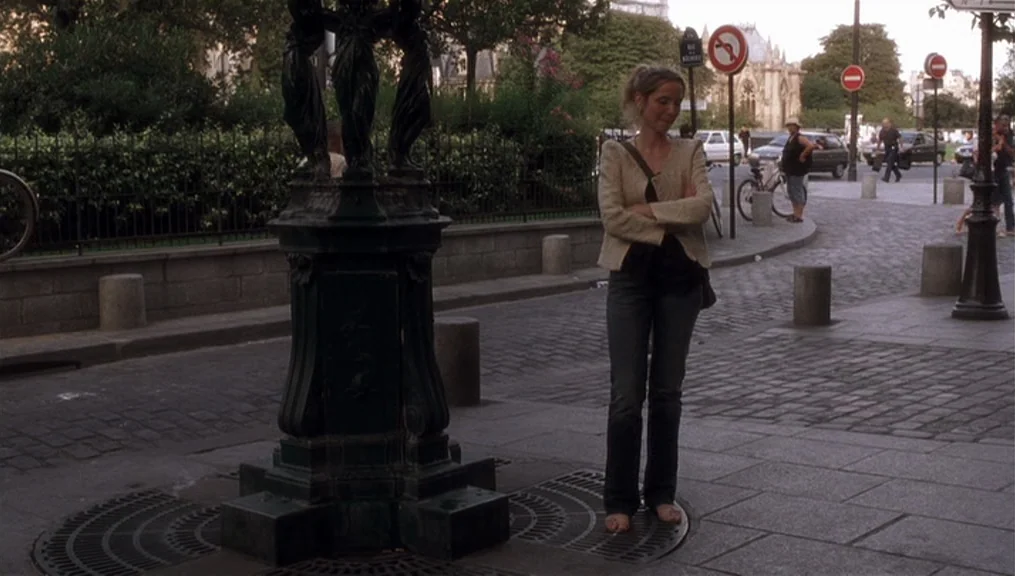 Before Sunset (2004) movie still: fullbody — A European cobblestone plaza features a decorative metal fountain base and stone bollards. A young…