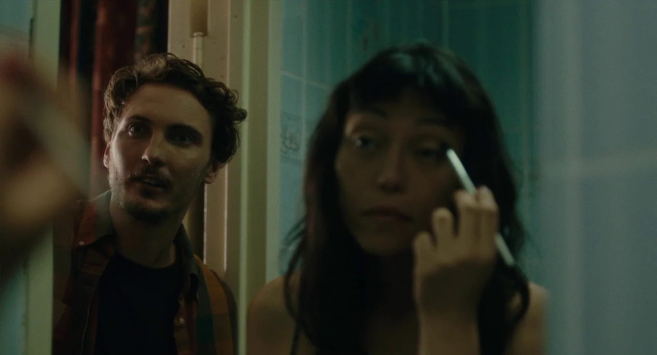 Lingua Franca (2019) movie still: medium — A tiled bathroom interior featuring light blue wall tiles and a reflective surface. A man leans over to…