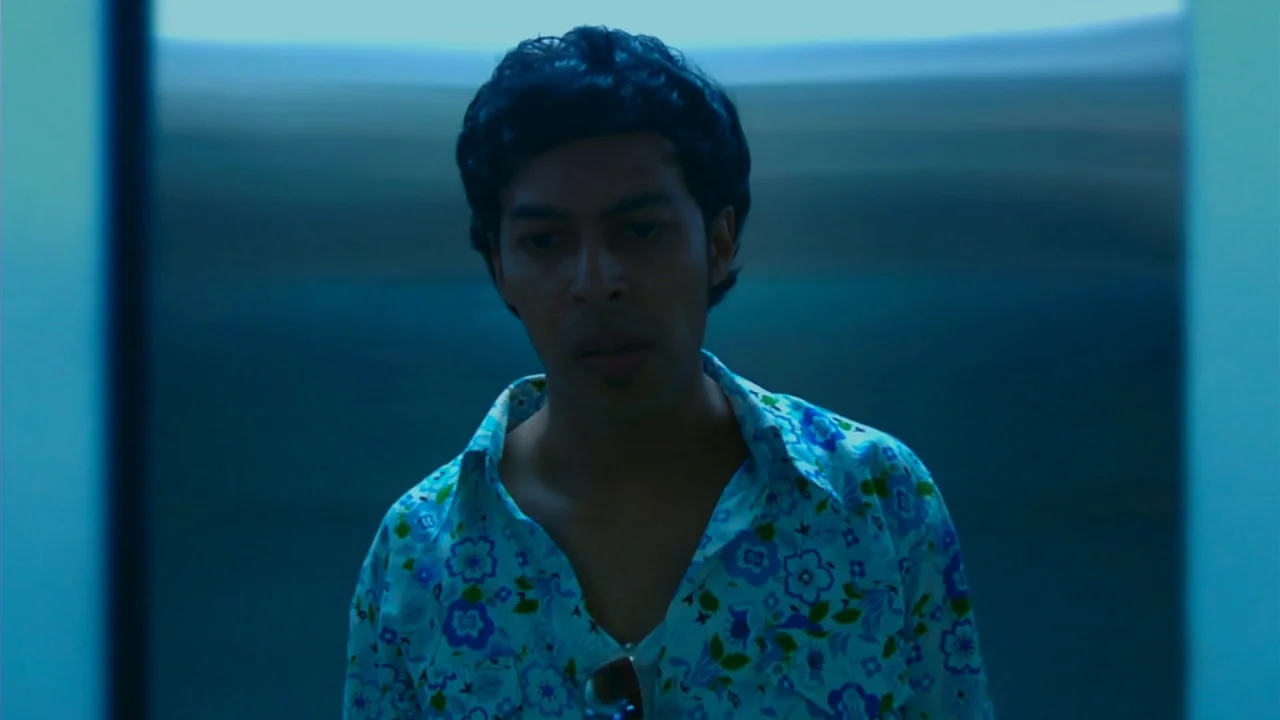 Merantau (2009) movie still: medium — A man stands inside a narrow space with plain, dark-blue wall panels. He gazes straight ahead while wearing a…