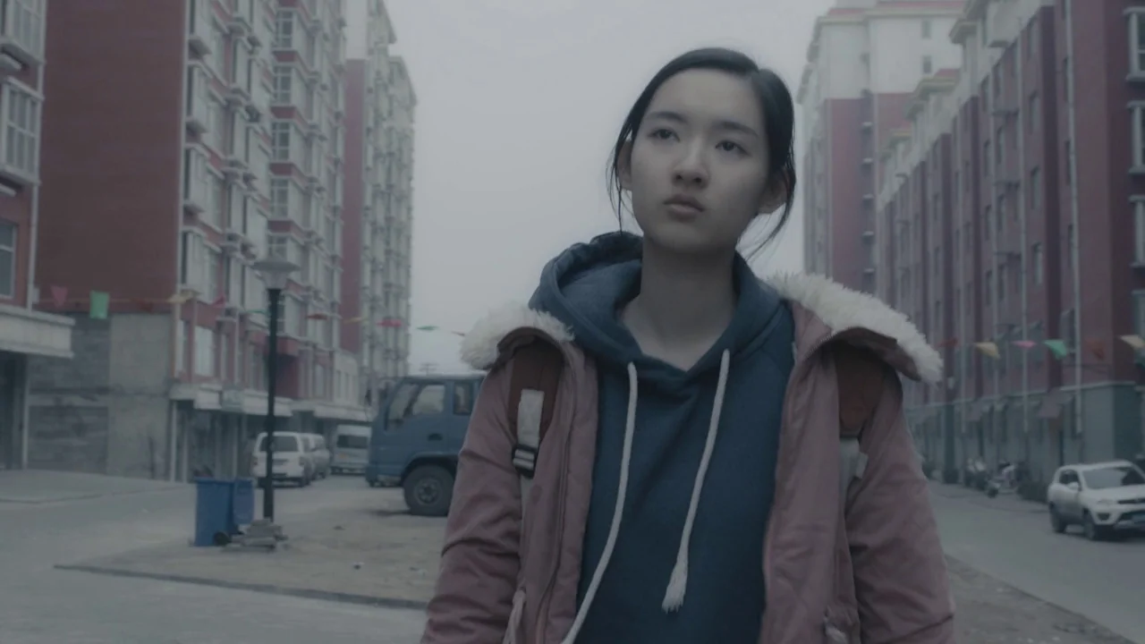 An Elephant Sitting Still (2018) movie still: medium — A residential block with tall, faded red apartment buildings stands under an overcast sky. A…