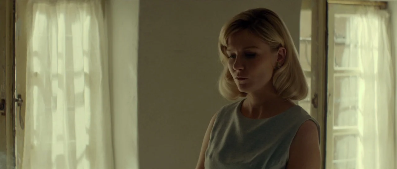 The Two Faces of January (2014) movie still: medium — A bright room features two tall windows flanked by sheer white curtains. A blonde woman stands…