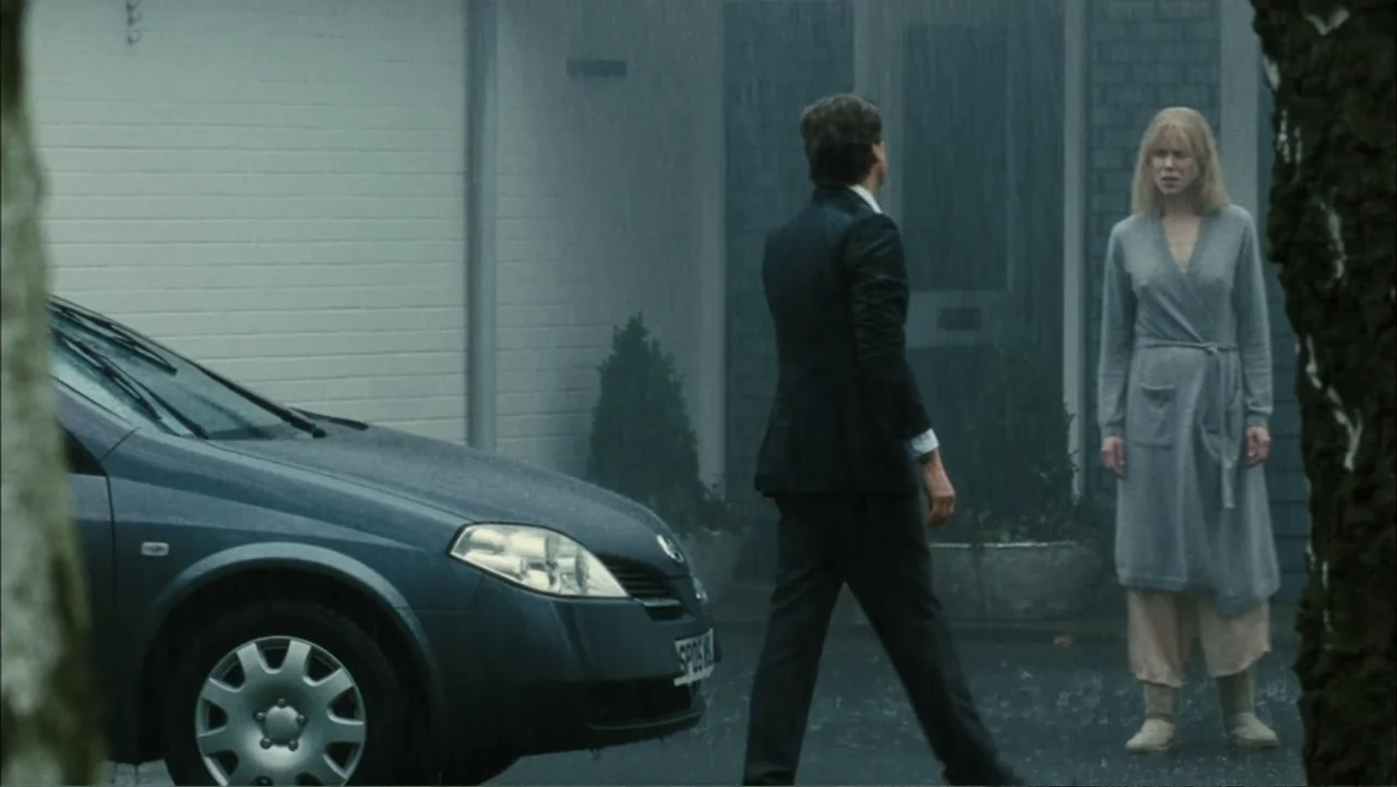 Before I Go to Sleep (2014) movie still: fullbody — A rain-slicked suburban driveway features a dark sedan parked near a modern residential…