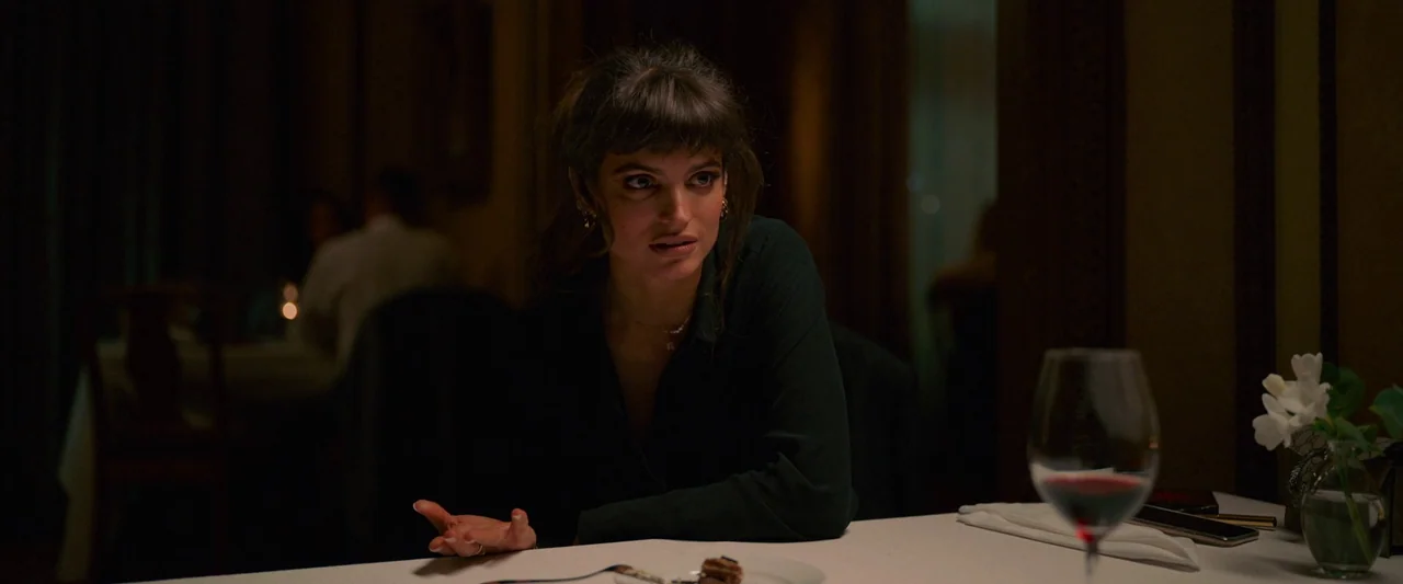 Triangle of Sadness (2022) movie still: medium — A dimly lit upscale environment with white tablecloths and dark surroundings. A young woman…